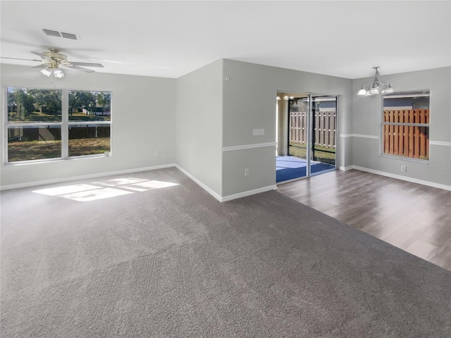 unfurnished room with ceiling fan with notable chandelier and dark colored carpet