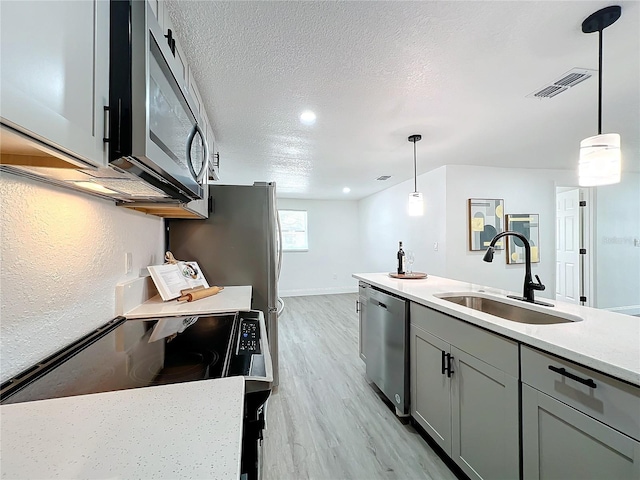 kitchen featuring sink, hanging light fixtures, light wood-type flooring, a textured ceiling, and stainless steel appliances