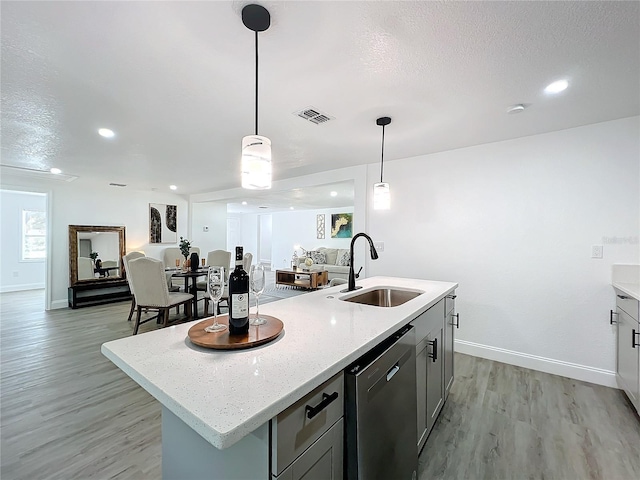 kitchen featuring pendant lighting, sink, light stone countertops, an island with sink, and stainless steel dishwasher