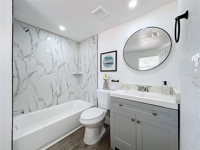 full bathroom with tiled shower / bath, hardwood / wood-style flooring, vanity, toilet, and a textured ceiling