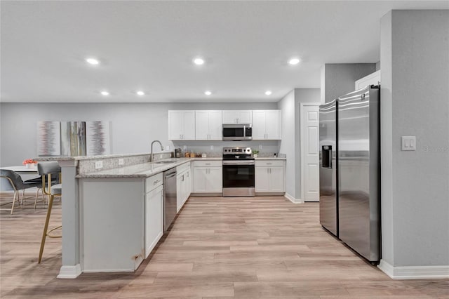 kitchen featuring a kitchen breakfast bar, a peninsula, stainless steel appliances, white cabinetry, and a sink