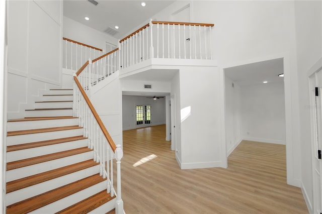 staircase featuring baseboards, visible vents, a high ceiling, and wood finished floors