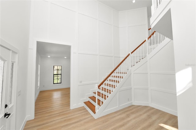 stairway with wood finished floors, a towering ceiling, and a decorative wall