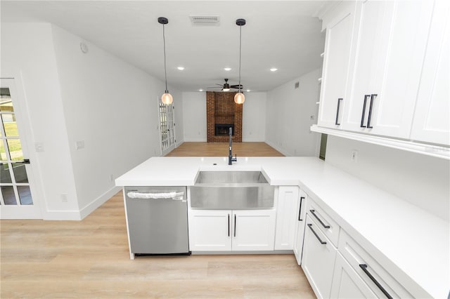 kitchen featuring light countertops, stainless steel dishwasher, white cabinets, a sink, and a peninsula