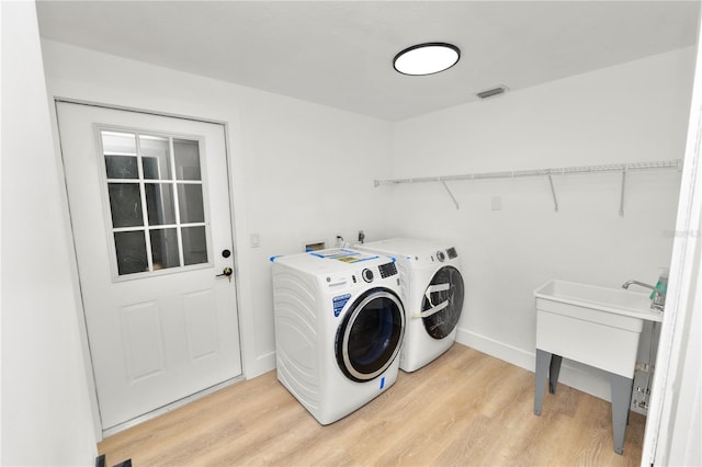 clothes washing area with laundry area, separate washer and dryer, a sink, visible vents, and light wood-type flooring