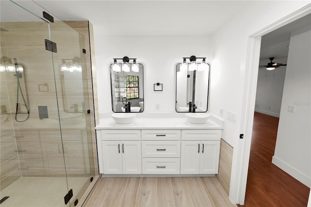 bathroom with double vanity, a sink, a shower stall, and wood finished floors