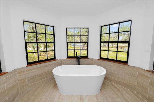 full bathroom with tile walls, a freestanding bath, and wainscoting