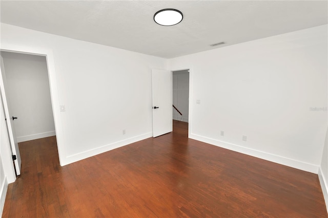 unfurnished room featuring dark wood finished floors, visible vents, and baseboards