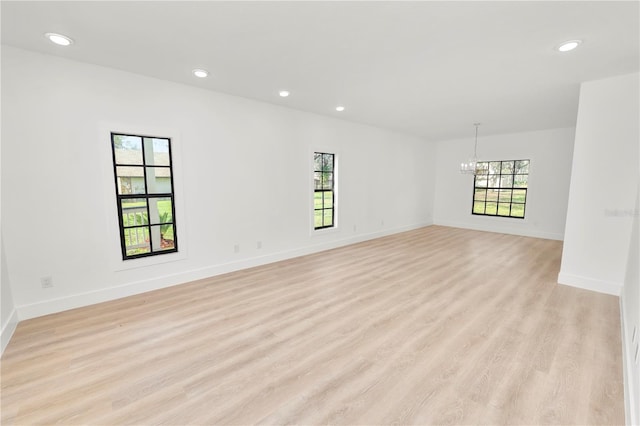 empty room featuring an inviting chandelier, plenty of natural light, and light wood finished floors