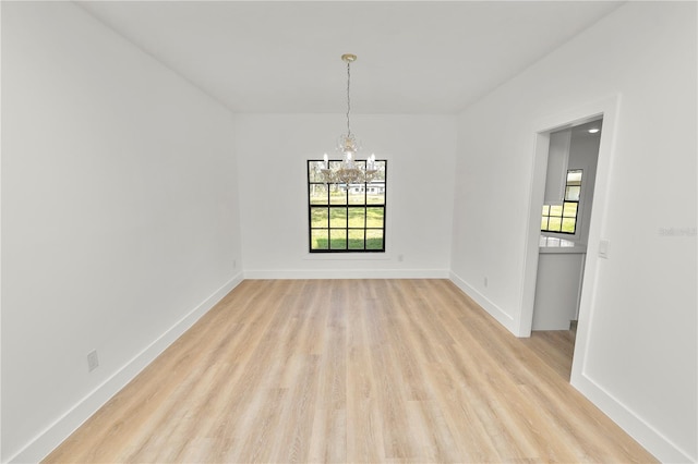 empty room featuring a notable chandelier, baseboards, a wealth of natural light, and light wood-style floors