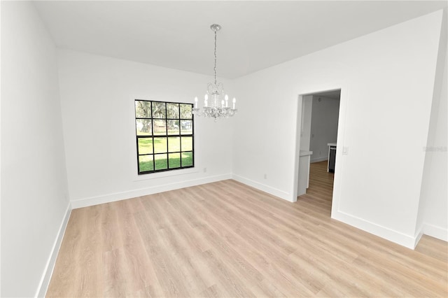 empty room featuring light wood-style flooring, baseboards, and a notable chandelier