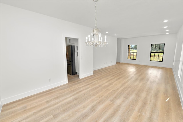 empty room featuring a notable chandelier, light wood finished floors, recessed lighting, and baseboards