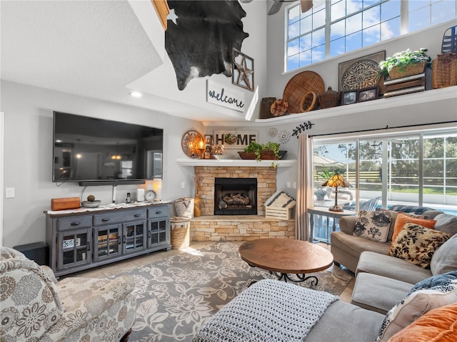 living room featuring light tile patterned flooring, a towering ceiling, a stone fireplace, and a wealth of natural light