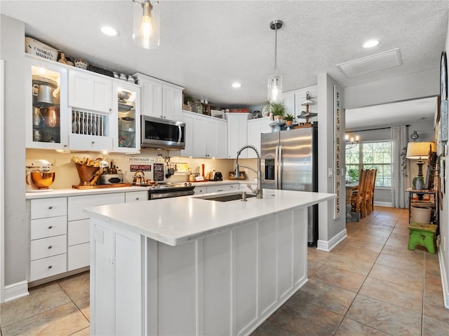 kitchen featuring sink, white cabinetry, hanging light fixtures, stainless steel appliances, and a center island with sink