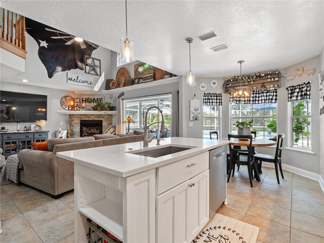 kitchen featuring sink, white cabinets, hanging light fixtures, a kitchen island with sink, and stainless steel dishwasher