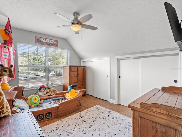 recreation room with light hardwood / wood-style flooring, a textured ceiling, vaulted ceiling, and ceiling fan