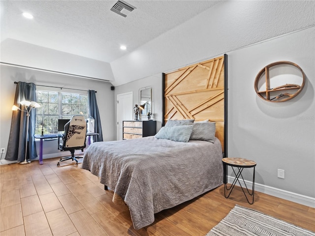 bedroom with hardwood / wood-style flooring, vaulted ceiling, and a textured ceiling