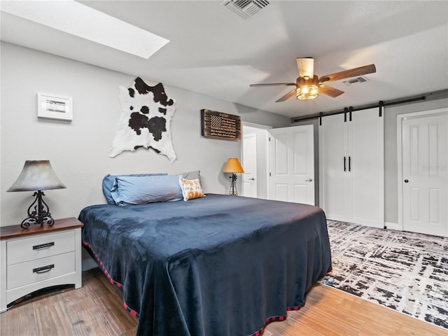 bedroom featuring a barn door, hardwood / wood-style floors, ceiling fan, and a skylight