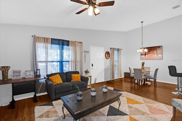 living area with lofted ceiling, ceiling fan with notable chandelier, wood finished floors, visible vents, and baseboards