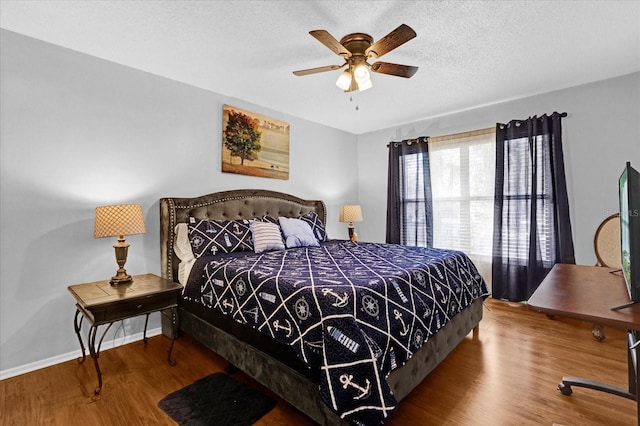 bedroom with a ceiling fan, a textured ceiling, baseboards, and wood finished floors