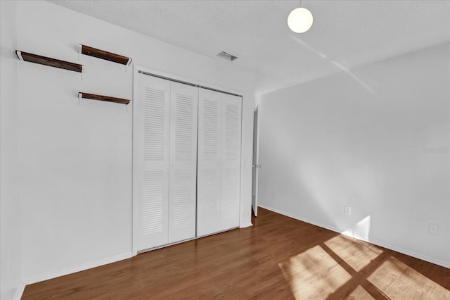 unfurnished bedroom featuring baseboards, a closet, visible vents, and wood finished floors