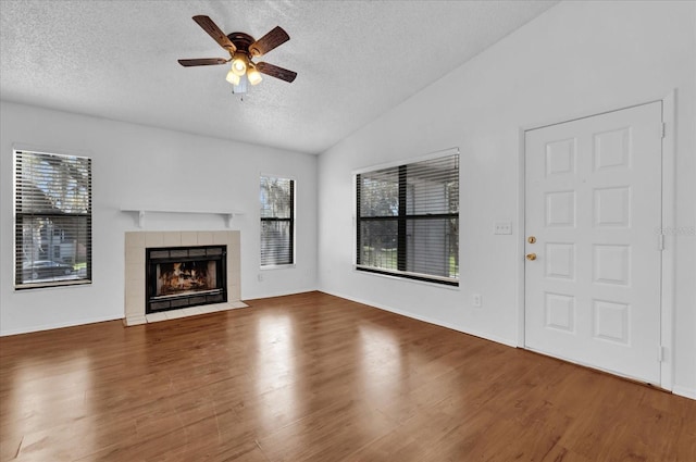 unfurnished living room featuring lofted ceiling, a textured ceiling, a tiled fireplace, and wood finished floors