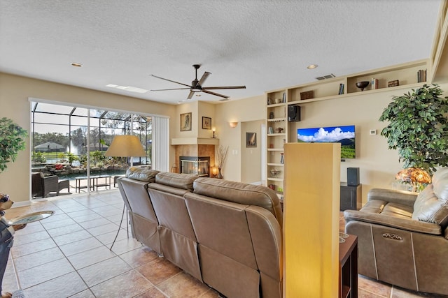 living room with a tile fireplace, light tile patterned floors, a textured ceiling, and ceiling fan