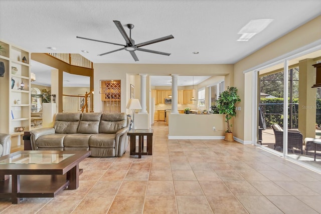 living room with light tile patterned flooring, built in shelves, a textured ceiling, ceiling fan, and decorative columns