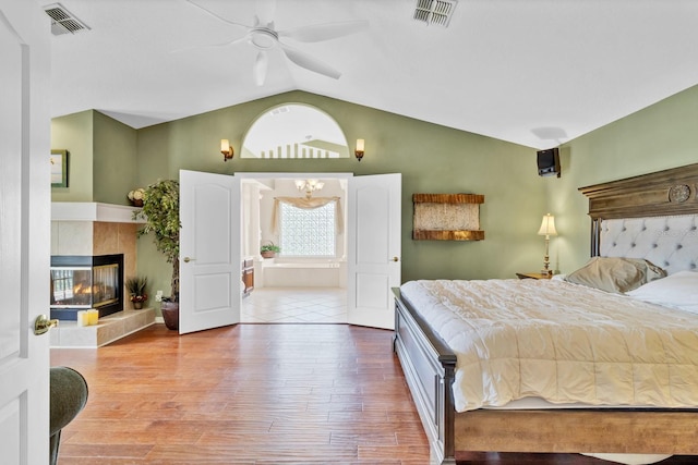 bedroom with a tiled fireplace, hardwood / wood-style flooring, vaulted ceiling, and ceiling fan