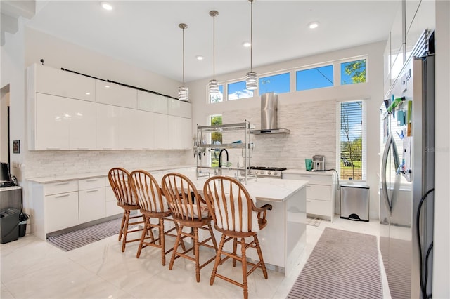 kitchen featuring stainless steel fridge, white cabinets, an island with sink, modern cabinets, and wall chimney range hood