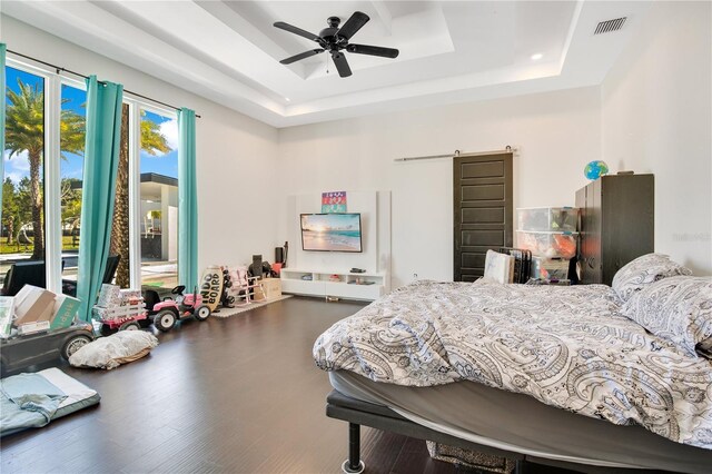 bedroom featuring a barn door, a raised ceiling, visible vents, and wood finished floors