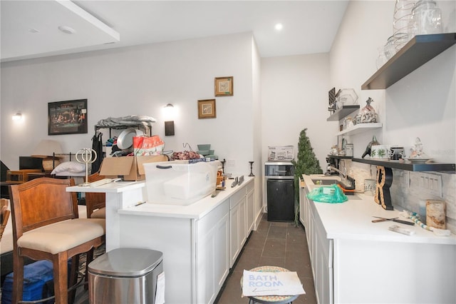 kitchen with dark tile patterned flooring, white cabinetry, a kitchen breakfast bar, light countertops, and open shelves