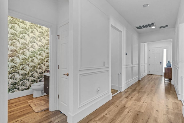 hallway with light wood-type flooring, visible vents, and wallpapered walls