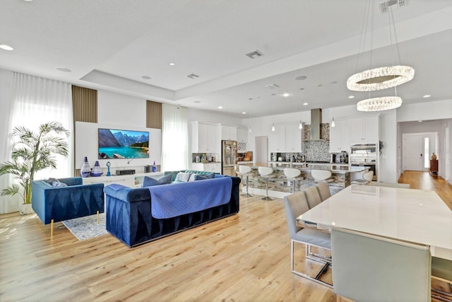 living area with a tray ceiling, recessed lighting, visible vents, and light wood-style floors