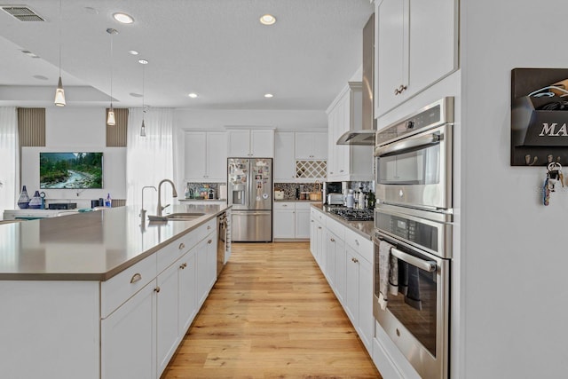 kitchen featuring visible vents, a sink, stainless steel appliances, light wood-style floors, and backsplash