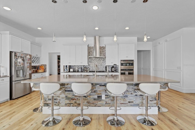 kitchen featuring tasteful backsplash, appliances with stainless steel finishes, a sink, wall chimney range hood, and a kitchen breakfast bar