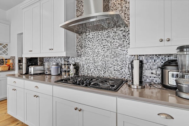 kitchen featuring wall chimney range hood, black gas stovetop, backsplash, and white cabinetry