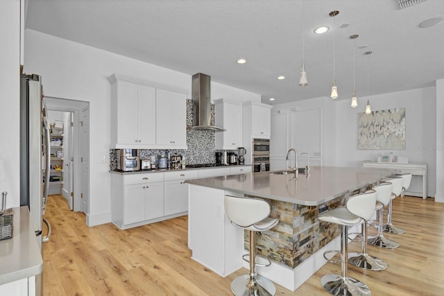 kitchen featuring decorative backsplash, a kitchen breakfast bar, a sink, and wall chimney exhaust hood