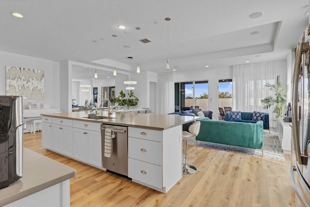 kitchen featuring visible vents, open floor plan, stainless steel dishwasher, white cabinetry, and a sink