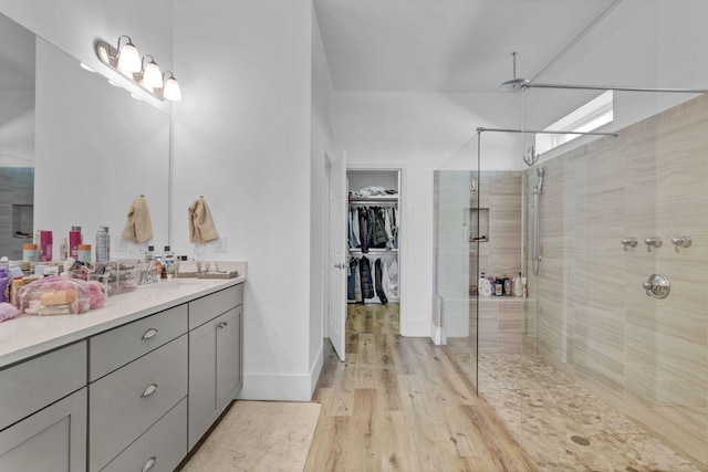 full bath featuring a spacious closet, a stall shower, vanity, wood finished floors, and baseboards