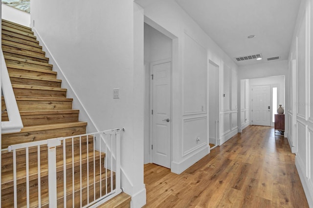 corridor featuring stairs, wood finished floors, visible vents, and a decorative wall