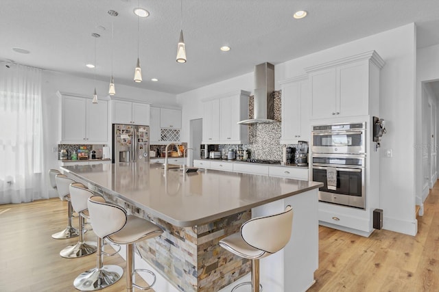 kitchen featuring wall chimney exhaust hood, appliances with stainless steel finishes, a kitchen breakfast bar, a large island with sink, and a sink