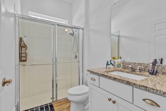 bathroom featuring wood finished floors, a shower stall, toilet, and vanity