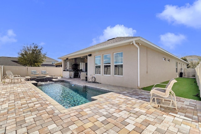 view of swimming pool featuring a patio area, a fenced backyard, a pool with connected hot tub, and an outdoor kitchen