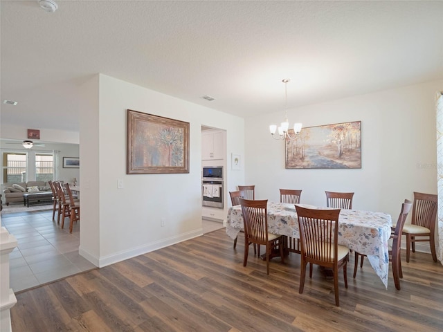 dining area with a textured ceiling, ceiling fan with notable chandelier, visible vents, baseboards, and dark wood finished floors