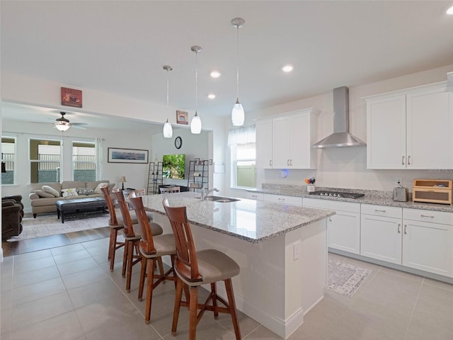 kitchen with pendant lighting, white cabinetry, wall chimney range hood, and an island with sink