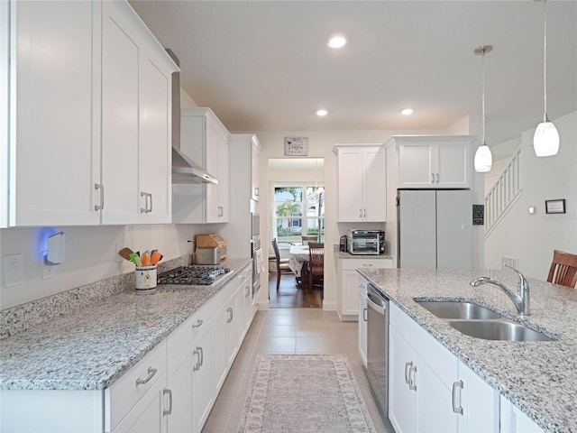 kitchen with a sink, white cabinets, hanging light fixtures, appliances with stainless steel finishes, and light stone countertops