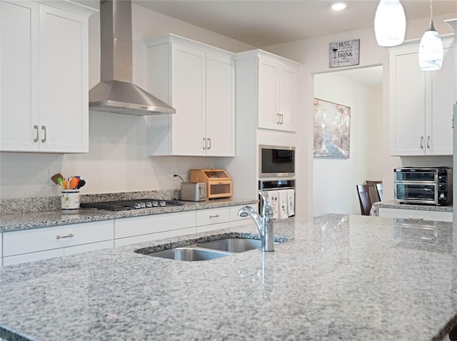 kitchen with a sink, white cabinetry, wall chimney range hood, appliances with stainless steel finishes, and decorative light fixtures