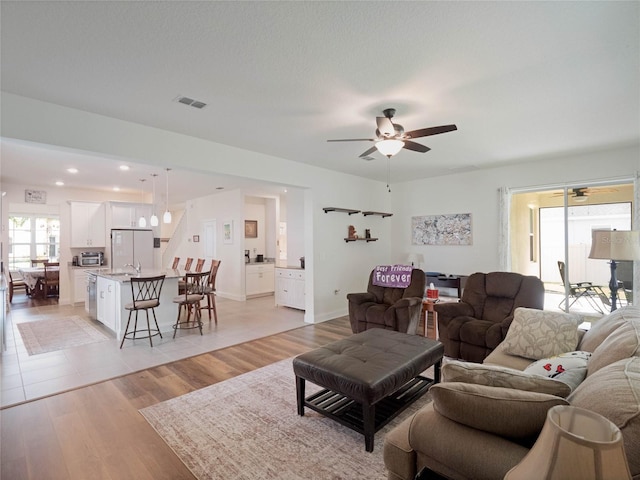 living area with a toaster, visible vents, baseboards, ceiling fan, and light wood-type flooring