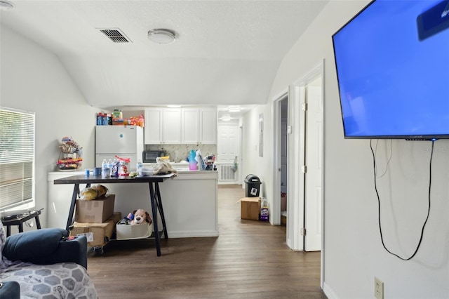 kitchen with dark wood-style flooring, visible vents, white cabinetry, vaulted ceiling, and freestanding refrigerator